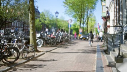 Obraz premium Blurred image of amsterdam street with bicycles, trees, and buildings featuring bokeh effect, capturing a typical urban scene in the netherlands.
