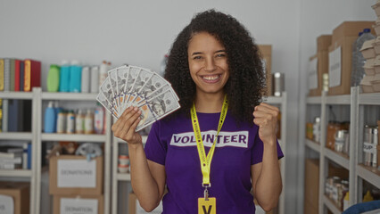 Woman smiling in a volunteer center holding a fan of us dollar bills while surrounded by charity...
