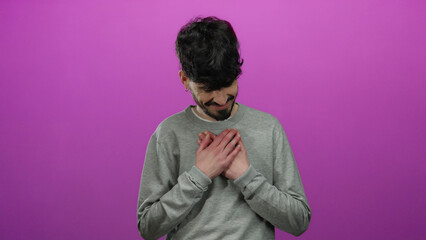 Young man in gray sweater stands against isolated pink background looking sincere and thoughtful.