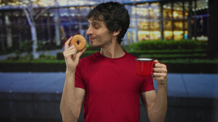 Fototapeta premium Man wearing red t shirt holding donut and mug on urban city street at night under street lights; happiness.