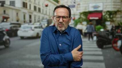 Mature man in blue shirt looking cold while walking in busy urban street surrounded by blurred...