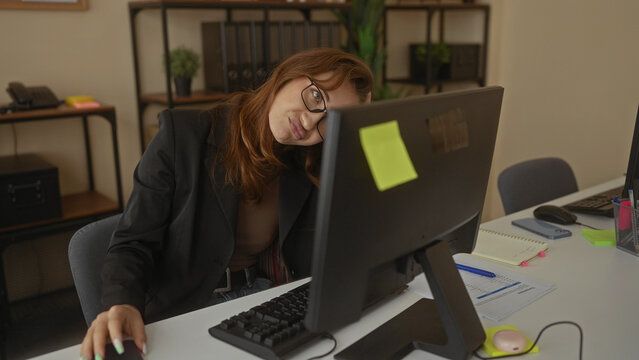 Caucasian woman in office looking stressed with computer and phone surrounded by work materials reflecting a busy workplace environment indoors. - Powered by Adobe