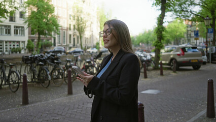 Woman using smartphone near amsterdam canals wearing glasses focusing on phone surrounded by...