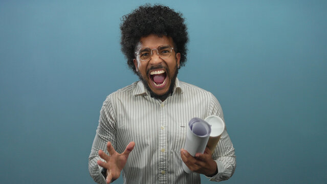 African american man shouting while holding blueprints in front of a blue wall background, expressing intense emotion, wearing striped shirt and glasses, isolated indoors. - Powered by Adobe