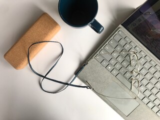 A tidy workspace scene with a laptop, a pair of glasses on a strap, a cork - like case, and a dark...