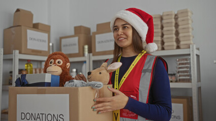 Woman organizing donations at charity center wearing santa hat sorting toys in festive indoor...