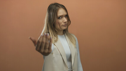 Young woman gestures come here with hand against isolated brown wall background conveying...