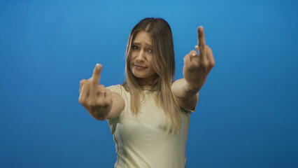Woman showing a displeased expression with a cheeky gesture against a bright blue background,...
