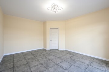 empty room with beige walls, grey tile flooring, a white door, and a modern ceiling light