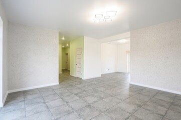 Bright, empty room with gray tile floor. Textured walls and modern ceiling light. Freshly painted interior