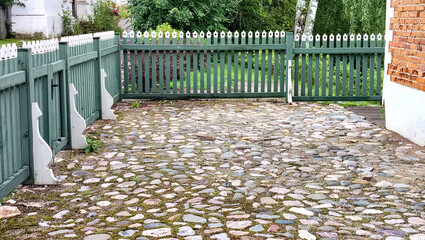 A neatly manicured farmyard, cobbled and enclosed by a wooden fence