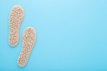 New light soft natural sheep wool insoles on light blue table background. Pastel color. Closeup....