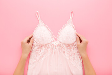 Young adult woman hands holding and showing new silk lace nightgown on light pink table background....