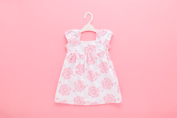 White dress with pink flowers on hanger on light pink table background. Pastel color. Closeup. Baby...