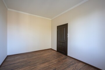 empty room with wooden floor, beige walls, white ceiling and a dark wooden door