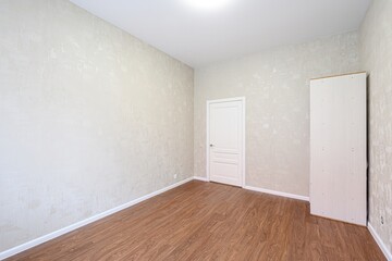 empty room with light beige walls, wooden floors, a white door, and a white unfinished cabinet in the corner