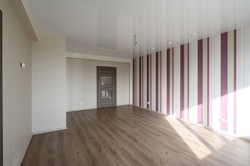 Bright, empty room with wood floors, striped wallpaper, and a modern door. Light streams in, highlighting the clean, minimalist design