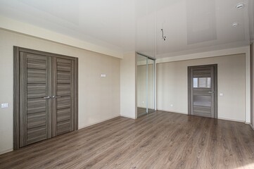 empty room with wooden floors and light walls. There are several wooden doors, a sliding mirror wardrobe, and a white ceiling with recessed lighting