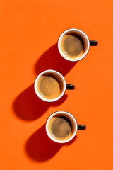 Three coffee mugs arranged neatly on a vibrant orange background, showcasing rich brews that evoke warmth and comfort.