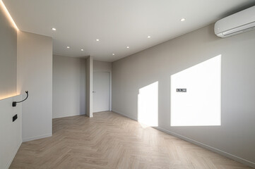 modern room featuring a herringbone wood floor, beige walls with indirect lighting, and sleek black sconces and outlets. Recessed ceiling lights add to the minimalist aesthetic