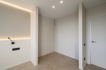 minimalist room corner featuring light beige walls, recessed lighting, wood-patterned flooring, and a modern wall-mounted lamp. Clean lines and neutral tones define the space