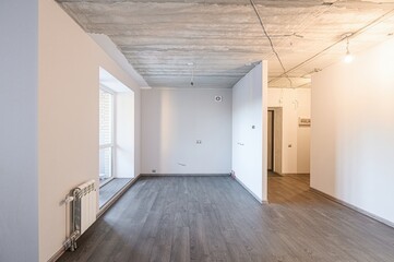 bright room under renovation with bare concrete ceiling, gray wood-look flooring, white walls, and...