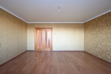 An empty room with wood laminate flooring and patterned wallpaper. A pair of wooden doors are at...