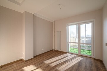 Empty room with wood flooring, beige walls, and a window showing a bright exterior. A radiator stands near the window