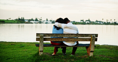 Back view, lake and couple on park bench on vacation, holiday and hug for bonding. Embrace, man and...