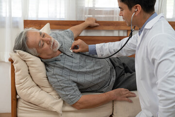 Obraz premium Doctor health checkup elderly patient and using stethoscope listen to heartbeat while lying on sofa at home. Retirement health care and life insurance concept