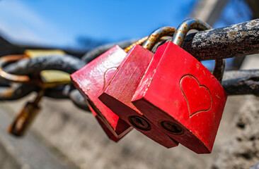 Padlock with heart symbol hanging on a wire fence against a clear blue sky in a serene outdoor...
