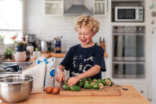 Happy curly haired child cutting feijoa guava fruit in kitchen