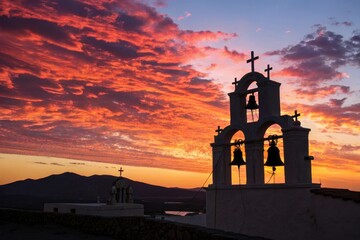 Silhouette of church bells with crosses against a vibrant orange and purple sunset sky over a mountain landscape