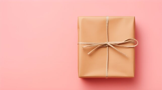 A neatly wrapped gift box sits against a soft pink backdrop, tied with rustic twine, evoking a sense of celebration and thoughtful giving.