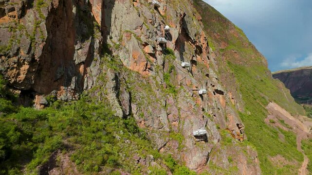 A breathtaking aerial approach reveals the Skylodge Adventure Suites' transparent glass pods dramatically suspended on a cliffside 1,300 feet above Peru's Sacred Valley.