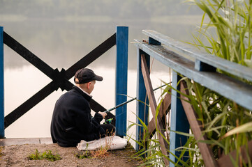 Close-up of a teenage boy fishing by a calm foggy lake in the early morning, fully focused and...