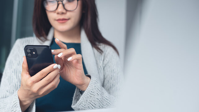 Asian business woman using smartphone, online working on laptop computer, surfing the internet, searching the information at office. Woman using mobile phone for online shopping and mobile banking