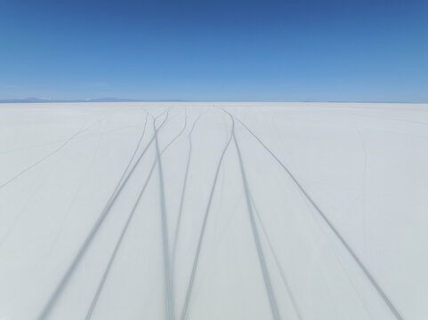 Aerial view of tire tracks etched across the endless white expanse of the salt flats under a clear blue sky, San Pablo de L&Atilde;&shy;pez, Potosi Department, Bolivia.
