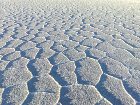 Aerial view of a vast, white expanse of hexagonal salt formations creating a mesmerizing geometric landscape under the bright sun, San Pablo de L&Atilde;&shy;pez, Potosi Department, Bolivia.