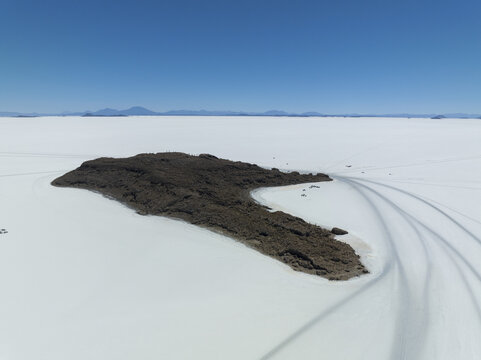 Aerial view of a dark, rocky outcrop standing starkly against the vast, blinding white expanse of the salt flats, San Pablo de L&Atilde;&shy;pez, Potosi Department, Bolivia.