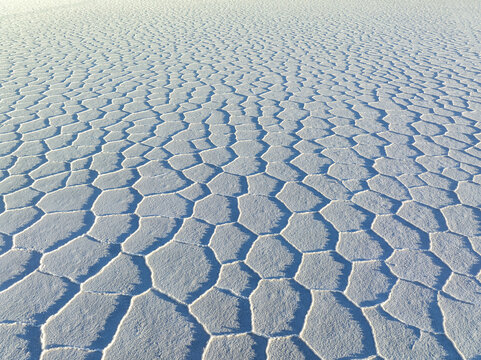 Aerial view of a vast expanse of stark, white salt flats stretch to the horizon, their cracked patterns creating a mesmerizing geometric tapestry, San Pablo de L&Atilde;&shy;pez, Potosi Department, Bolivia.