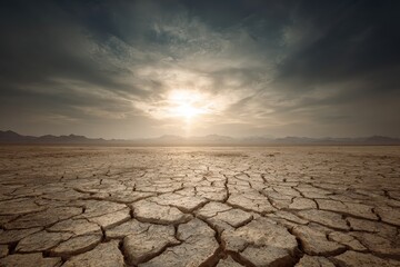 Cracked, arid landscape under a cloudy sky, with sunlight piercing through. Dry soil texture