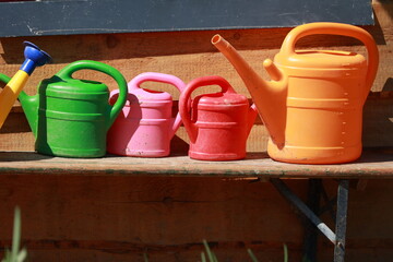 Naklejka premium A row of plastic garden watering cans sit on a wooden bench