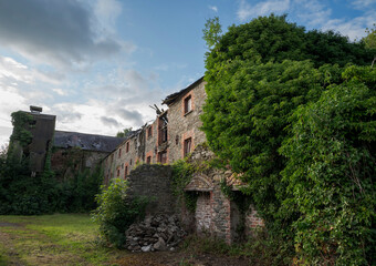 Ruins of an abandoned, industrial building shows crumbling stone and brick, with boarded-up windows and ivy climbing the surface. Photo taken in Inniskeen, County Monaghan, Ireland