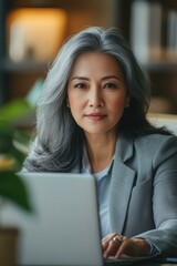 30s middle-aged woman using computer technology for financial bank work online. Mature Asian professional it specialist businesswoman working on laptop pc sitting at desk in office. Portrait at camera