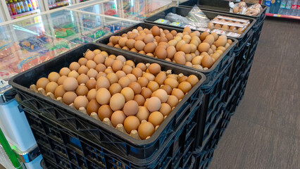 Brown eggs displayed in a supermarket on a black tray with green produce in the background.
