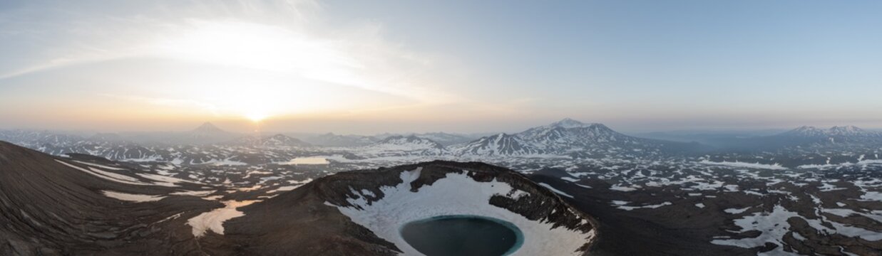 Aerial view of the contrasting dark volcanic crater rim with snow and a turquoise lake, set against the snowy landscape and rising sun, Yelizovo, Kamchatka Krai, Russia.