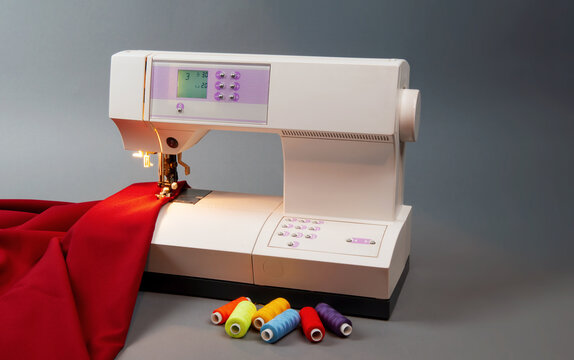 Sewing machine with red fabric, colorful threads on a gray background. Creative workspace concept for fashion, tailoring, or DIY sewing projects.
