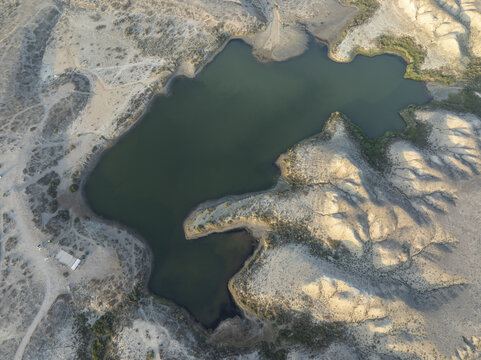 Aerial view of a serene lake nestled amidst arid, undulating hills under a soft, diffused light, creating a stark contrast between water and land, Kirpichny, Issyk-Kul Region, Kyrgyzstan.