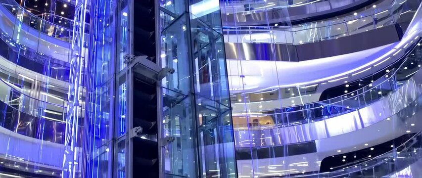 Modern glass-walled shopping mall with multiple levels and glowing blue accents